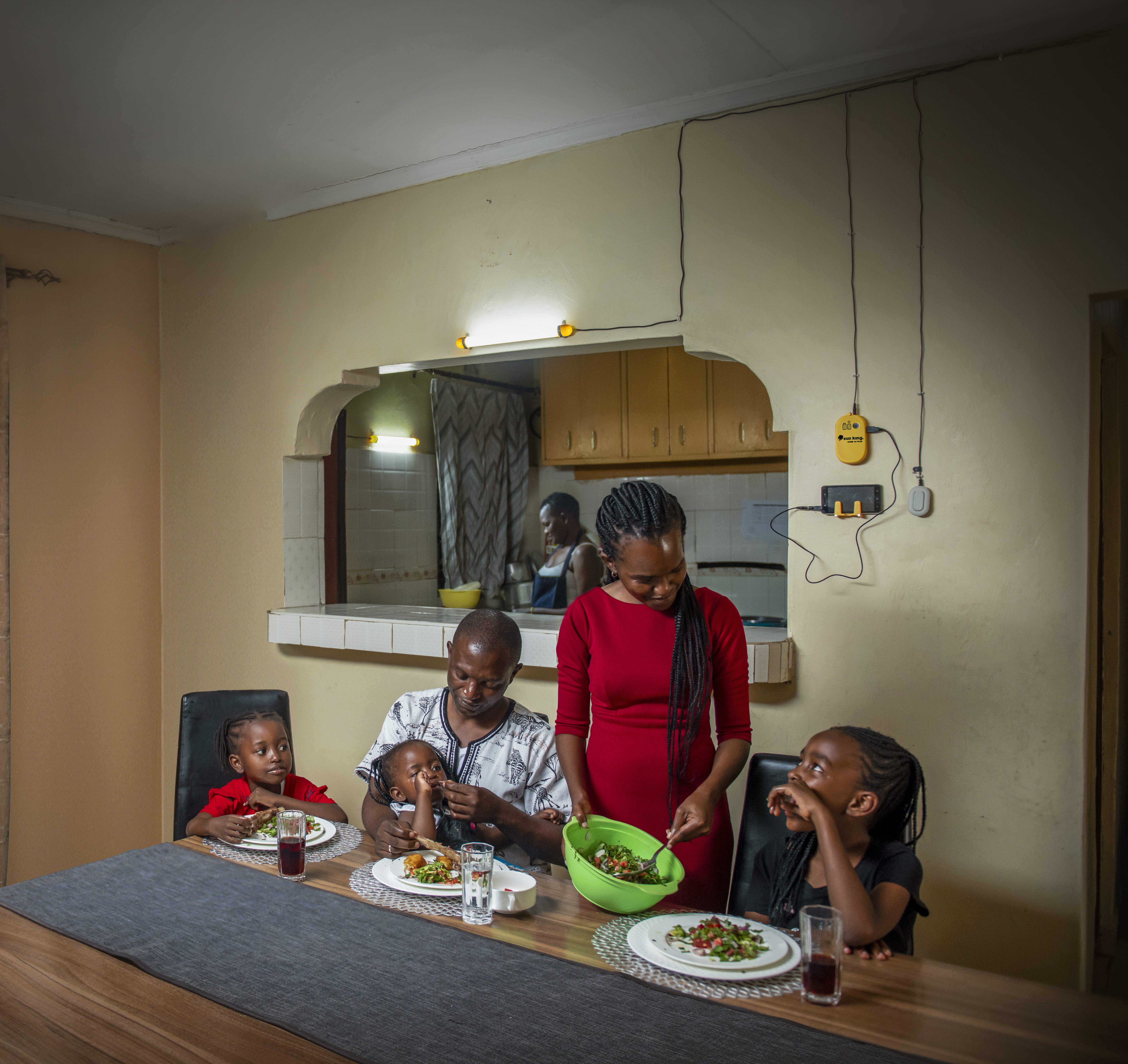 A family sits at the table in their kitchen, under the light of a Sun King solar home lighting system.