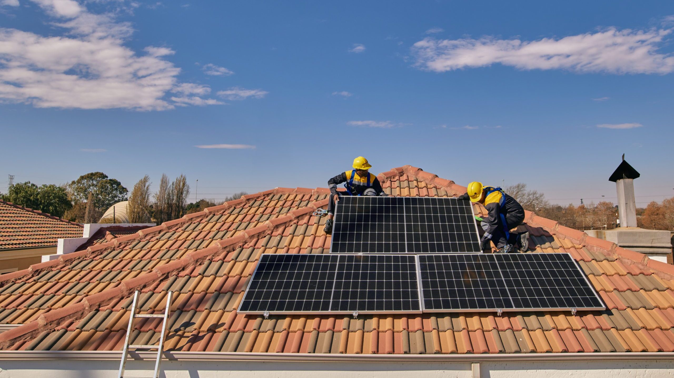 Workers on a tiled roof installing solar panels for a Sun King solar powered rooftop inverter system.