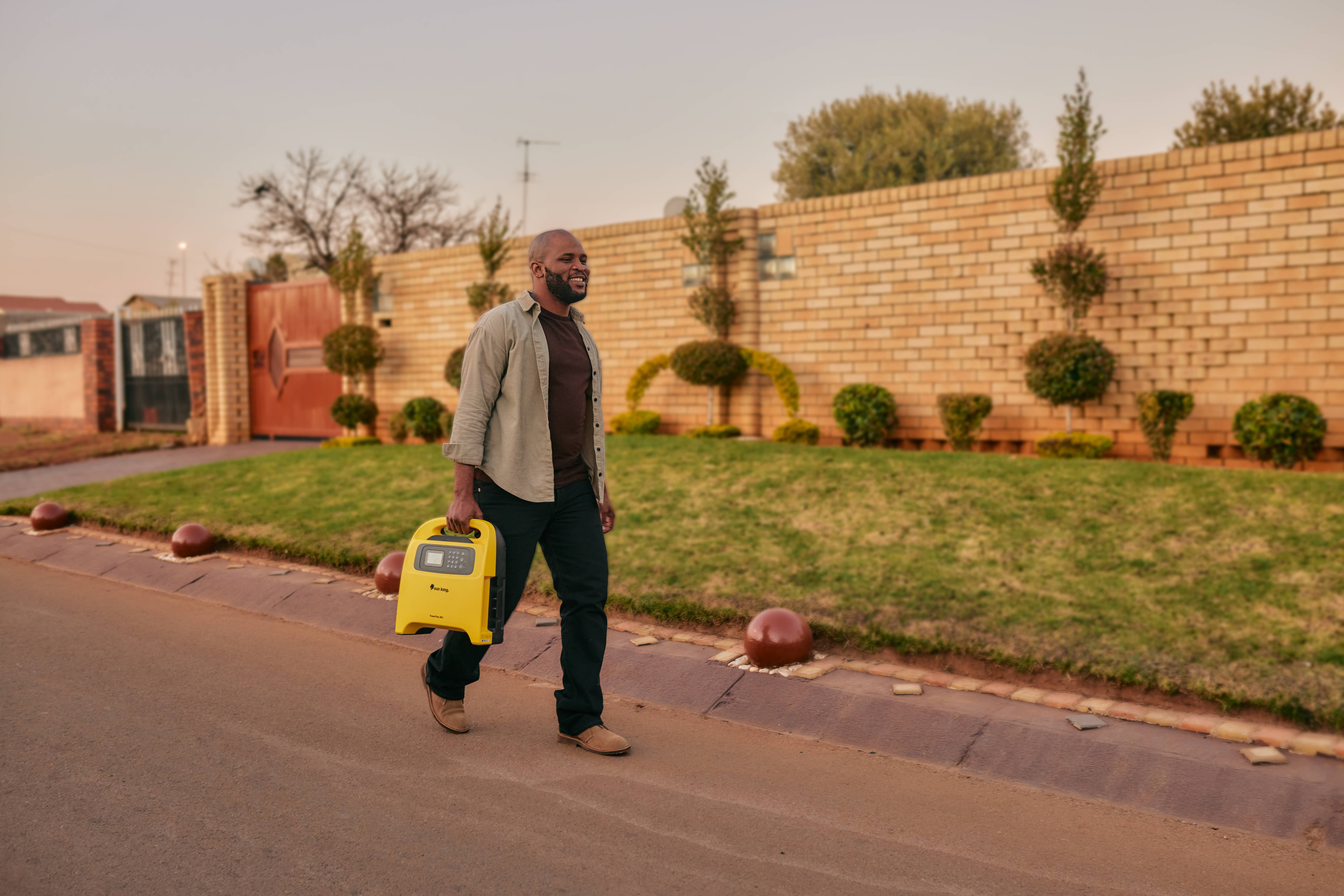 A man walks down a street carrying a Sun King PowerPlay Pro portable solar inverter system.