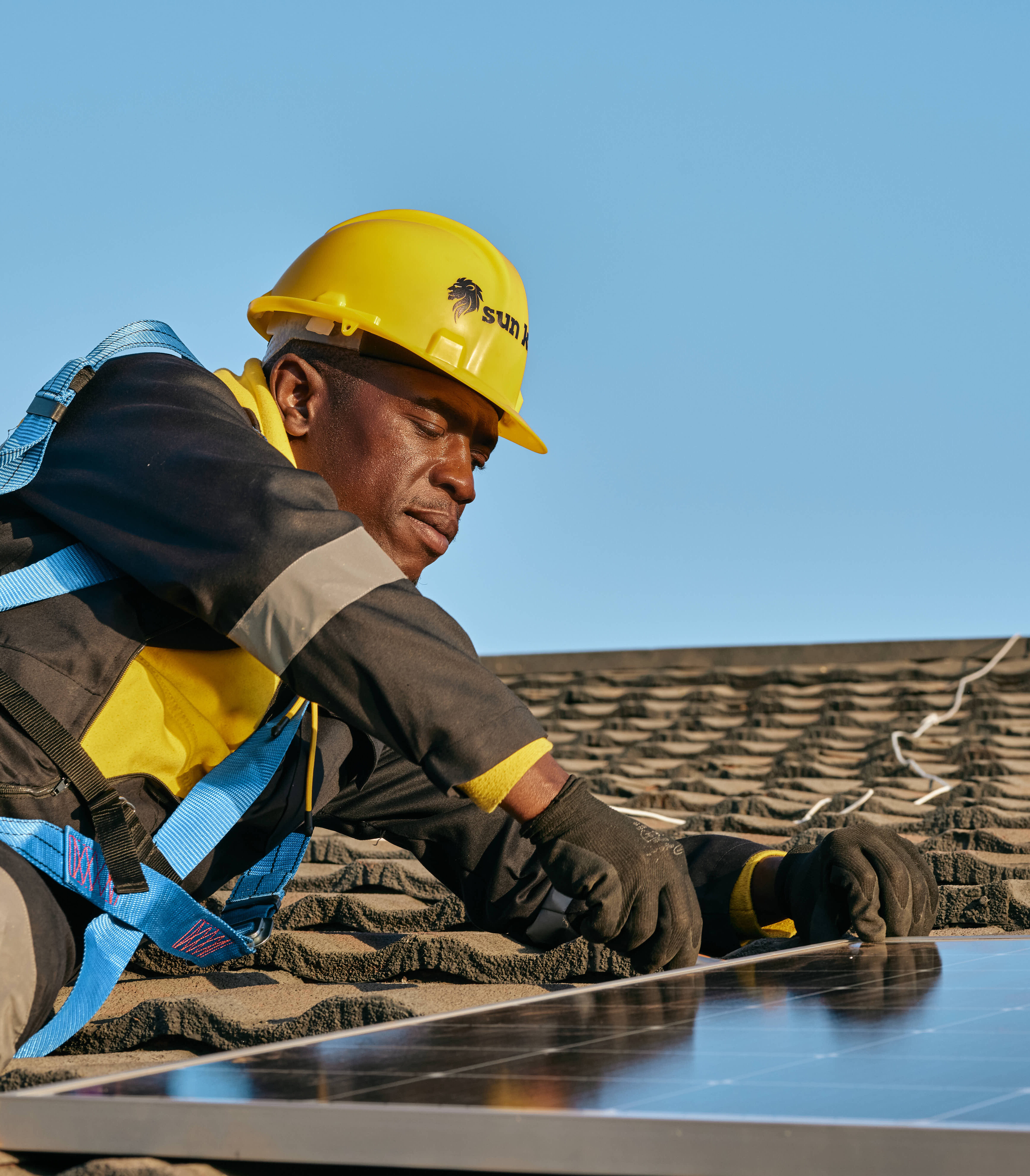 A Sun King Installer wearing protective gear fixes a PowerPlay Pro solar inverter system panel to the roof of a building.